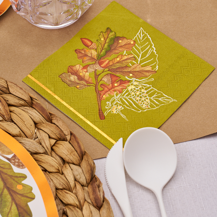 The Acorn and Oak Table Setting by Sophistiplate features a green napkin with autumn leaf and acorn accents, paired with a woven placemat, white cutlery, glassware, and a festive fall-themed plate for the perfect Thanksgiving tablescape.