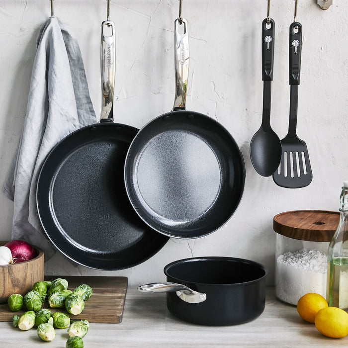 Black ceramic 5-piece cookware set hanging above a kitchen counter with assorted vegetables below.
