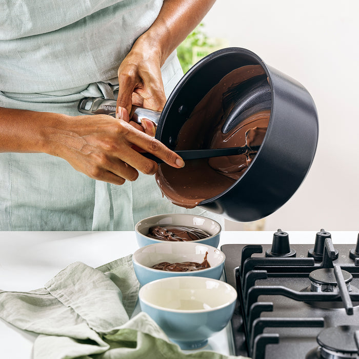 Melted chocolate being poured from a black ceramic nonstick pan from a 5-piece cookware set into bowls.