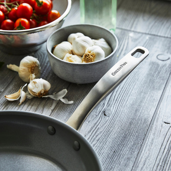The Chatham Ceramic Nonstick 10" Frypan sits on a wooden surface next to a bowl of garlic, loose cloves, and a colander of cherry tomatoes.