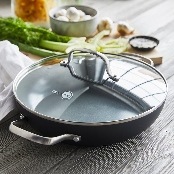 Ceramic nonstick everyday pan with lid on a table, surrounded by assorted fresh vegetables.