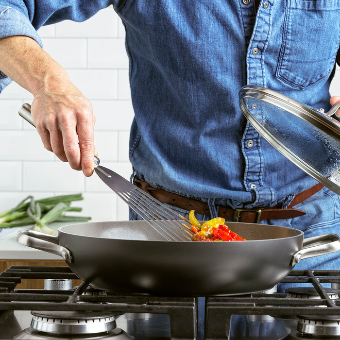 Person lifts glass lid on GreenPan Chatham ceramic nonstick 11-inch pan while cooking vegetables on the stove.