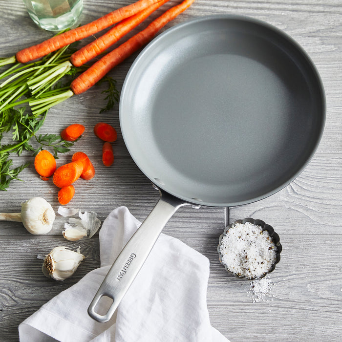 Gray ceramic nonstick 8-inch frypan with metal handle on a gray surface, next to carrots and garlic.
