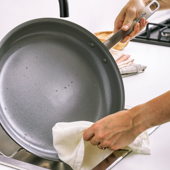 Person drying a Chatham ceramic nonstick 8-inch frypan with a white cloth over a sink.