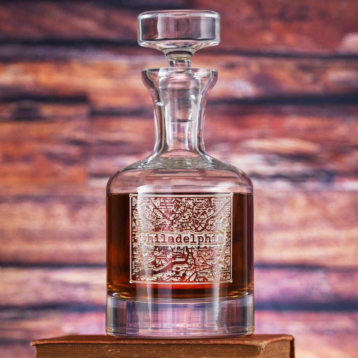 A glass spirits decanter with a faceted stopper, filled with amber spirit, deep-carved with a city street-map panel and the city name.