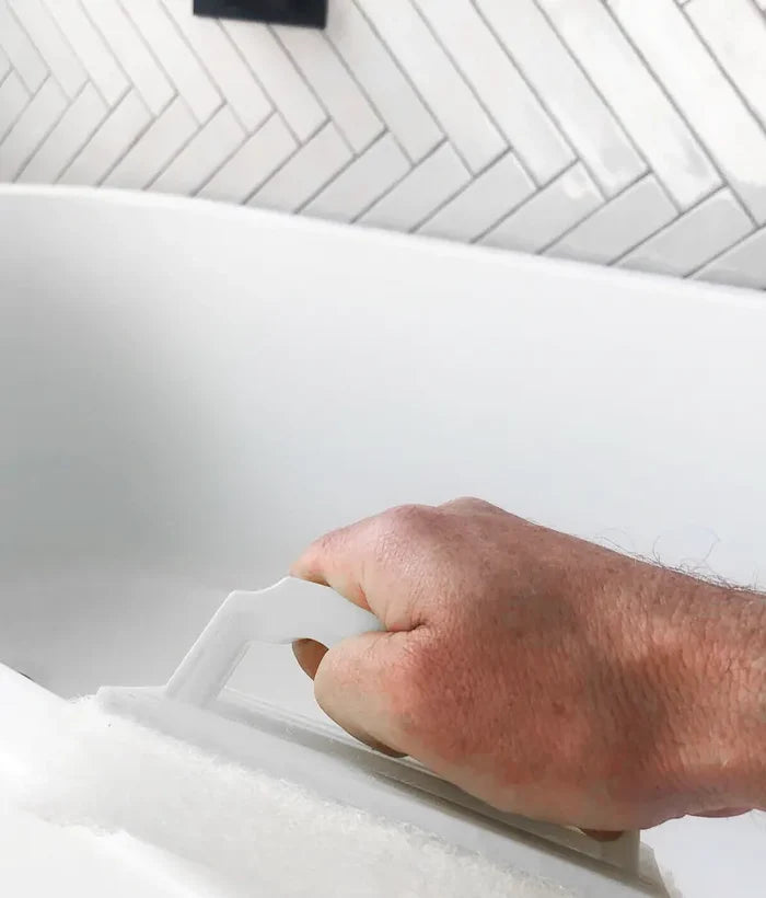 Hand using a white plastic tool on a white surface with a tiled wall in the background