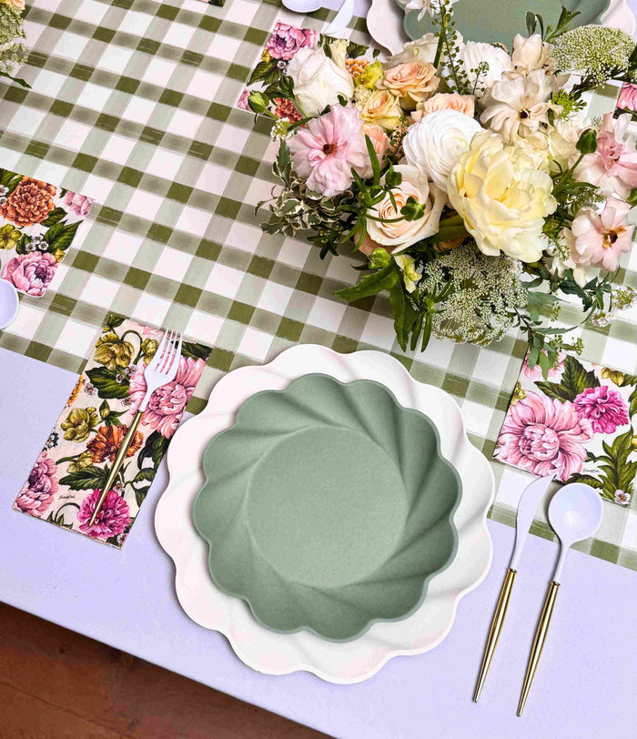 The Garden Rose Table Setting by Sophistiplate features a green and white checkered tablecloth, designer plates with scalloped edges, gold-handled cutlery, a floral napkin, and a pastel flower centerpiece.
