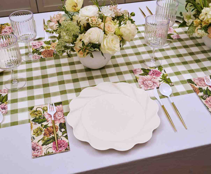 The Sophistiplate Garden Rose Table Setting features designer disposable plates, gold and white cutlery, floral napkins, and glassware on a green checkered cloth with elegant white and pale yellow blooms—perfect for a ready-made party.