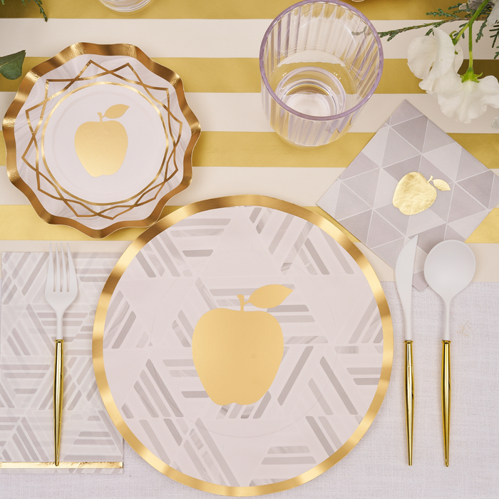 Create a sophisticated table setting using Sophistiplate’s Golden Apple Guest Towels (20-pack), featuring elegant gold and white plates adorned with a gold apple motif and delicate gold foil trim, paired with gold-rimmed utensils, glassware, and geometric napkins atop a striped floral-accented tablecloth.
