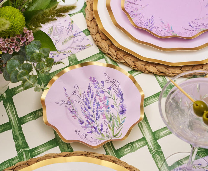 Scalloped pink plates with lavender florals and gold edges sit on woven placemats, accented by a green plant, a cocktail with olives, and the Hester & Cook Green Lattice Runner (20x25") for a fresh finishing touch.