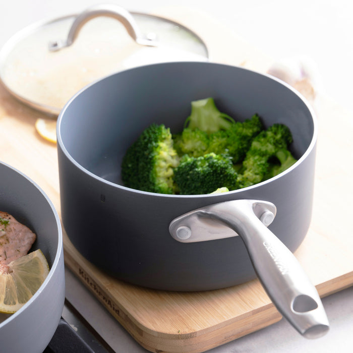 Ceramic nonstick saucepan set with lid next to a hard anodized aluminum cutting board on a countertop.
