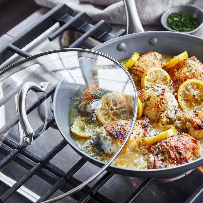 Chicken thighs and lemon with fresh herbs in a ceramic nonstick frypan with lid.