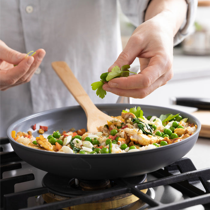 Vegetables, rice, and herbs cooking in a Lima ceramic nonstick frypan with lid on a stovetop.