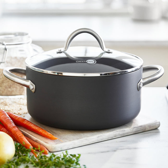 Gray ceramic stockpot with lid on a counter next to carrots, an onion, and leafy greens.