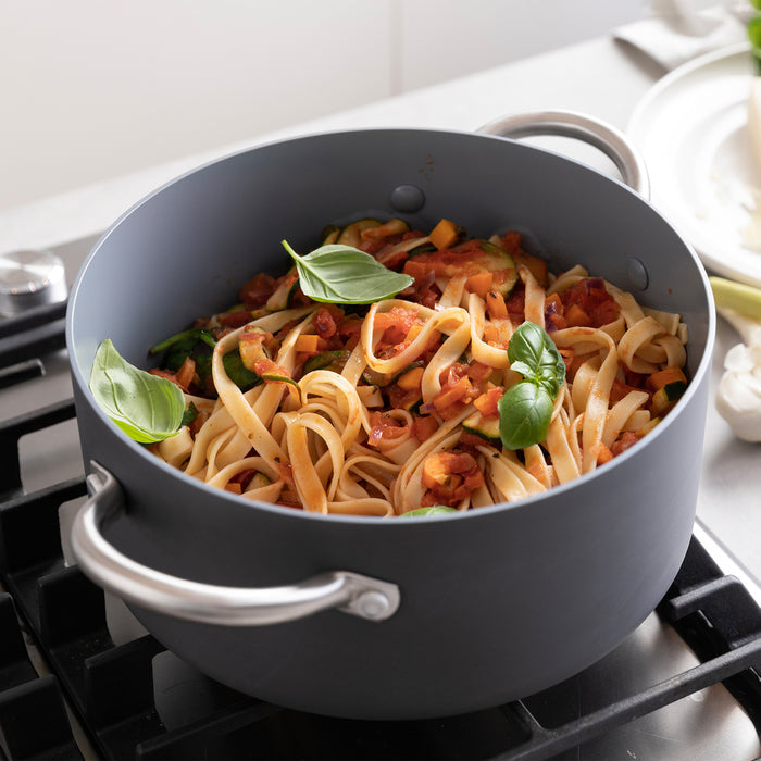 Green ceramic nonstick stockpot with lid on stove, filled with fettuccine pasta in tomato sauce and basil.