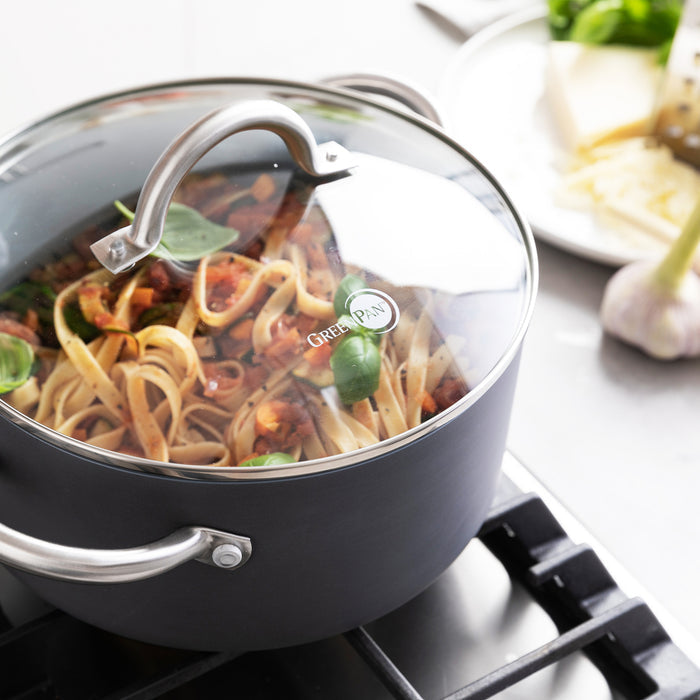 Pasta in red tomato sauce with basil cooking in a green ceramic 5-quart stockpot with glass lid.
