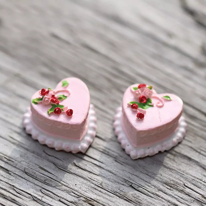 Two heart-shaped pink pastries with decorative elements on a wooden surface.