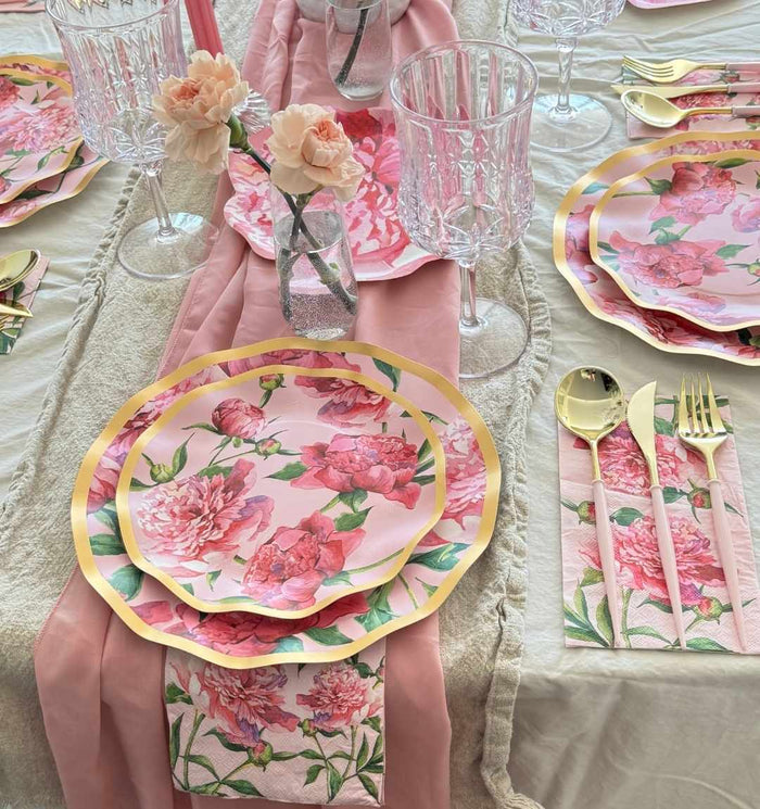 The Pink Peonies Table Setting by Sophistiplate LLC features designer disposable plates, matching napkins, a table runner, gold cutlery, crystal glasses, and pink flower vases on a cream-colored tablecloth.