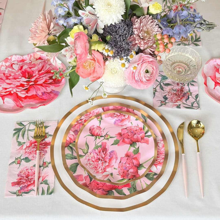 The Sophistiplate LLC Pink Peonies Table Setting includes designer floral plates with gold rims, gold and pink cutlery, and pink floral napkins, all beautifully arranged around a vibrant bouquet centerpiece.