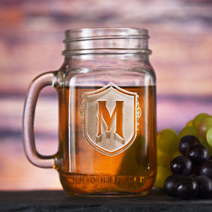 Mason jar mug with a handle, sand-carved with a single initial on an ornate shield.