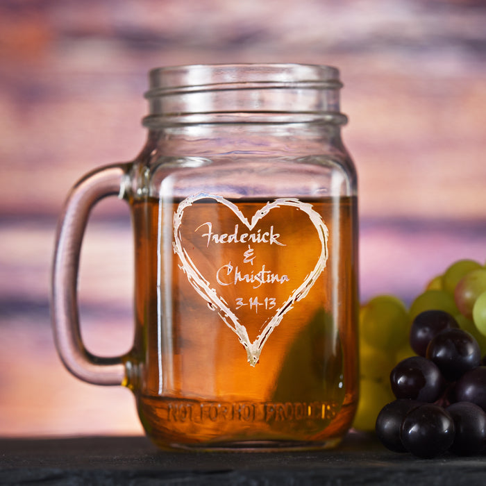 Mason jar mug with a handle, sand-carved with two names and a date inside a hand-drawn heart.